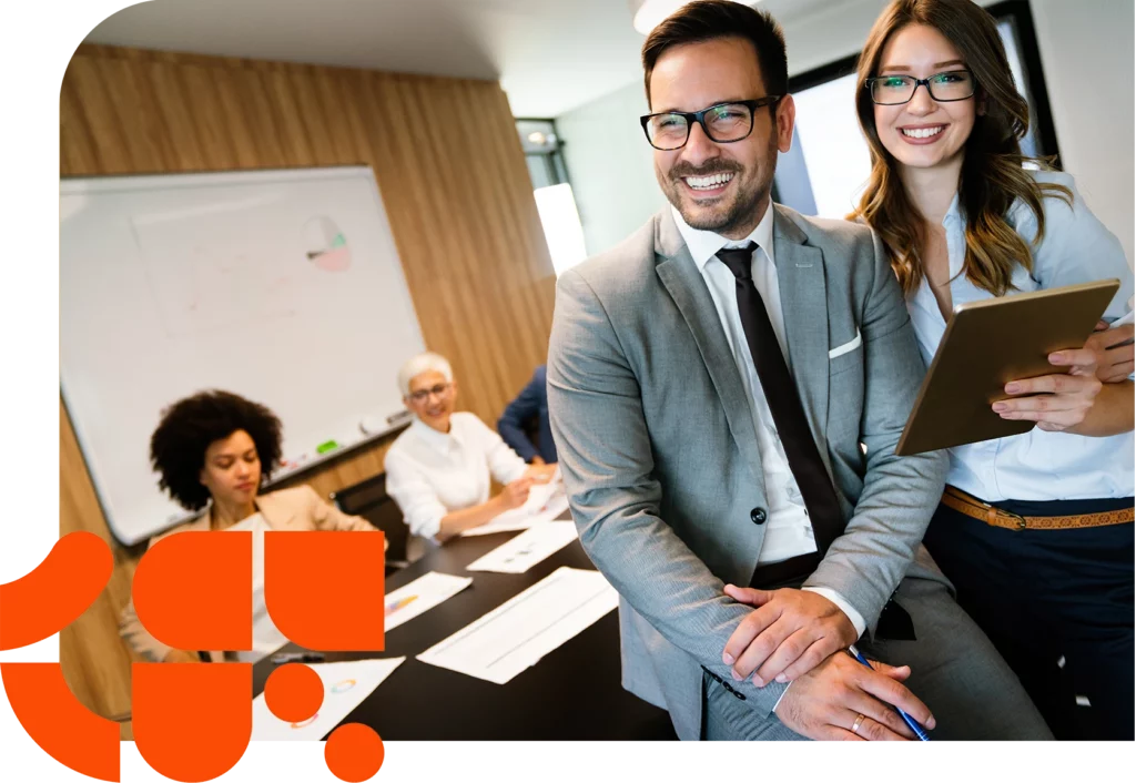 Two business people with a tablet are standing in front of a meeting team in the conference room.