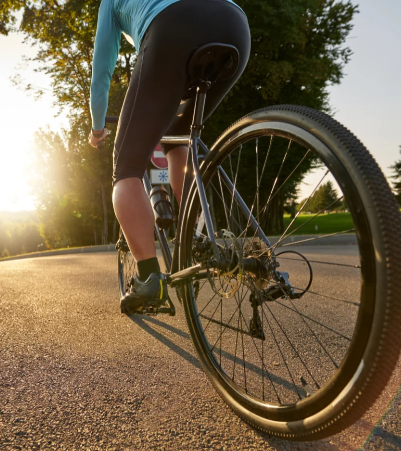 A male cyclist with a professional appearance rides through the park at sunset.
